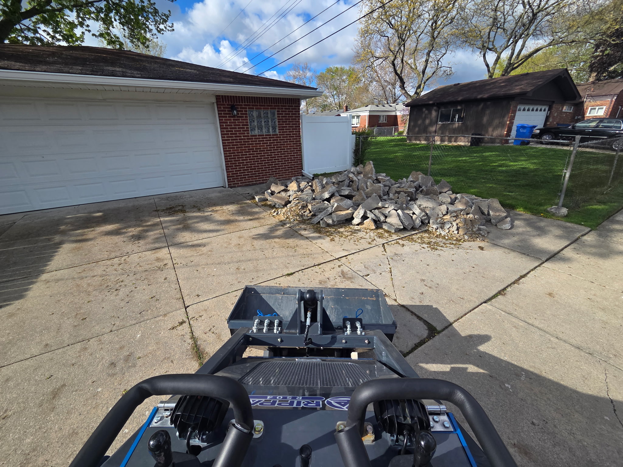 Mini skid steer removing broken concrete from a residential driveway in Michigan